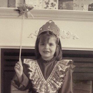 Portrait of MadJohn! as a child. She is a young white girl of about six years old, dressed in a frilly dress and toy tiara, holding a wand with a star on the end.