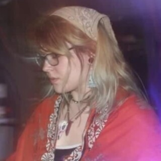 Photo of Spirit Tongues aka Dakota McIvor, a young white women with long blonde hair. She is wearing a red kimono with gold trim and a bandana over her hair.