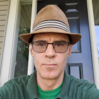 Headshot of poet Joe Bishop, a white man wearing a brown hat, square-shaped glasses, and a green golf shirt.