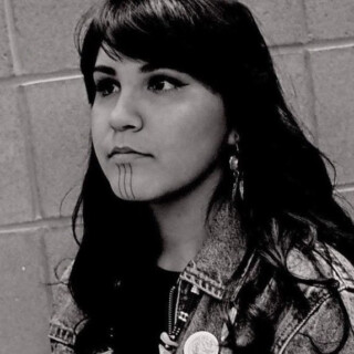 Portrait of poet Chasidy, an Indigenous woman with long dark hair and brown eyes. She is wearing a denim jacket and dark t-shirt.
